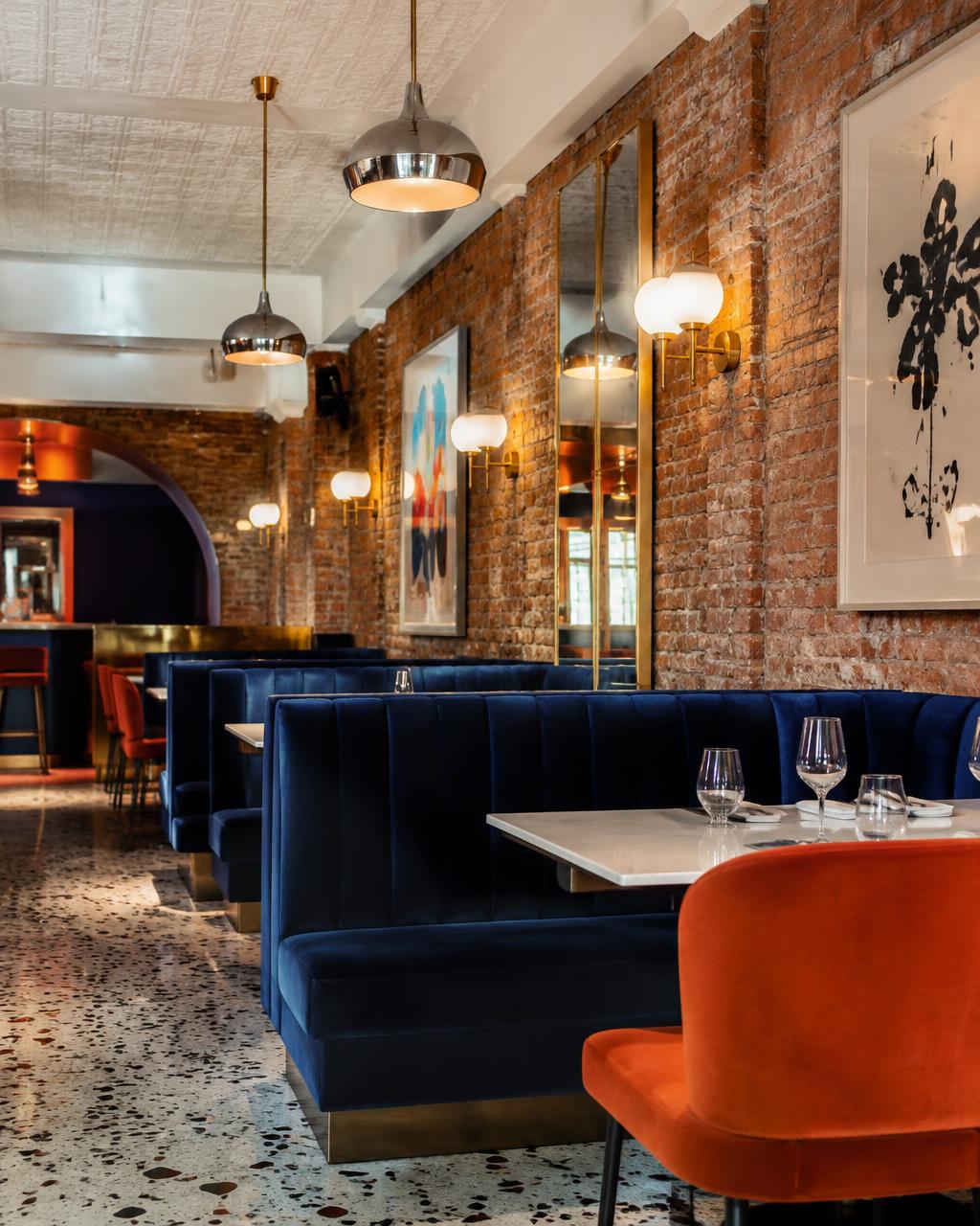 Restaurant with exposed brick, cobalt velvet banquettes and orange dining chairs