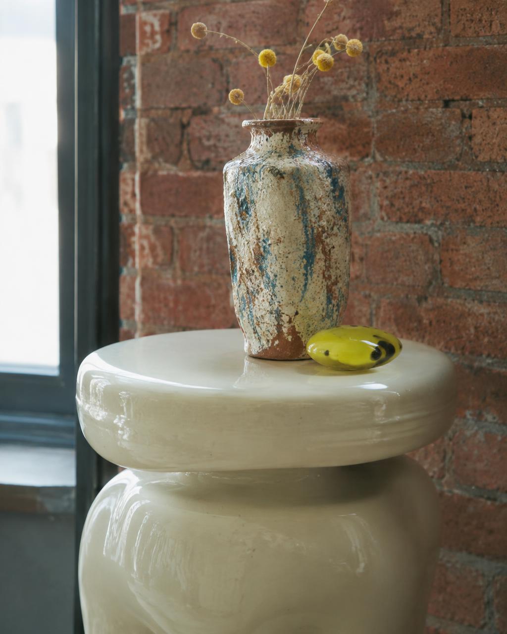 Sculptural glossy side table with ceramic vase against exposed brick